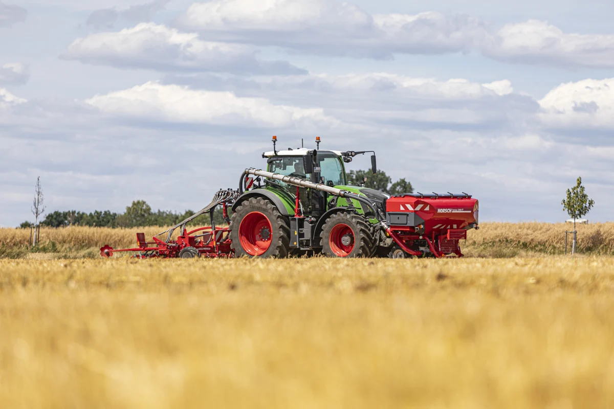 Sembradora Horsch Avatar SL enganxada al darrere d'un tractor verd, amb la tremuja frontal al davant del tractor, en un camp de rostoll