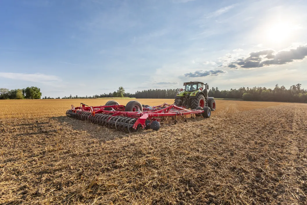 Cultivador Horsch Cruiser XL desplegat sobre rostoll, amb el tractor petit al fons i el cel amb núvols