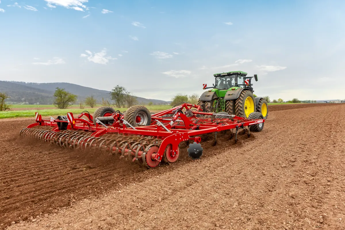 Cultivador Horsch Cruiser XL de gran amplada arrossegat per un tractor verd sobre terra acabada de treballar