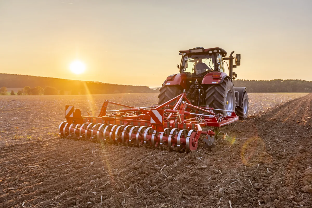 Cultivador Horsch Cruiser SL darrere d'un tractor al capvespre, amb el sol arran de l'horitzó