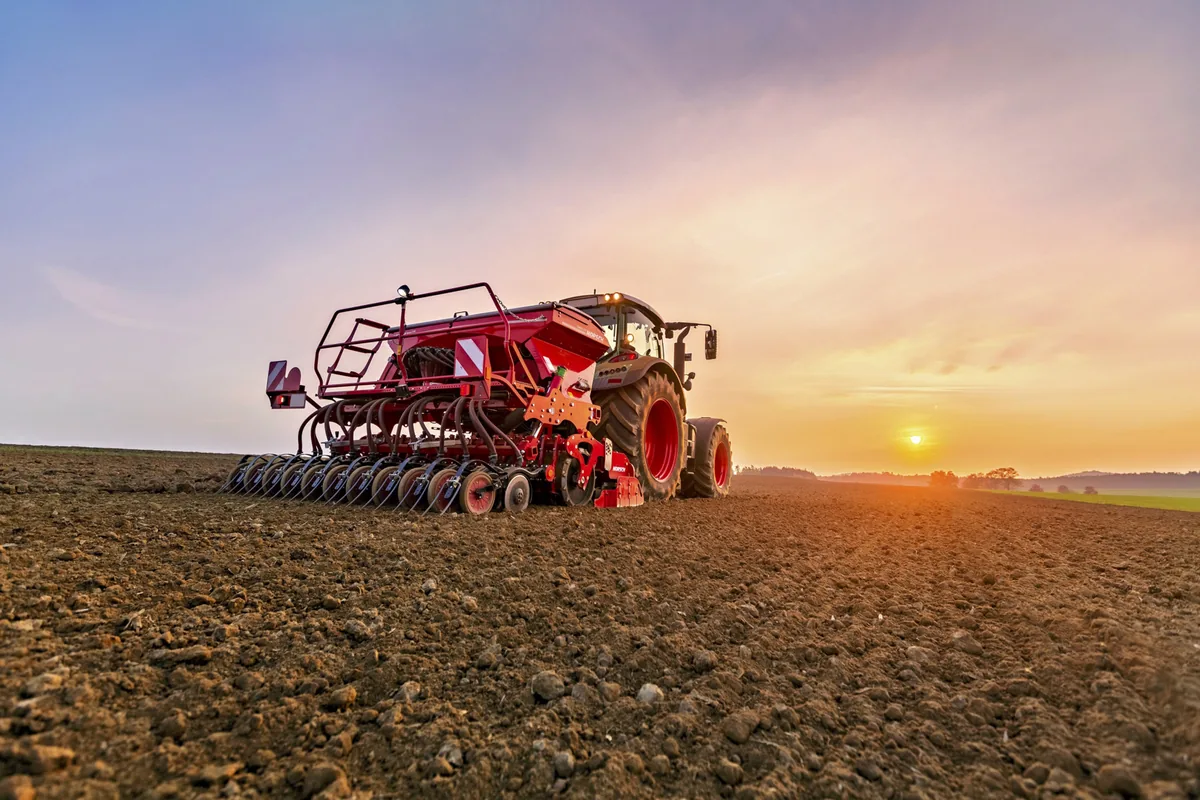 Sembradora Horsch Express KR darrere d'un tractor al capvespre, amb el sol arran de l'horitzó