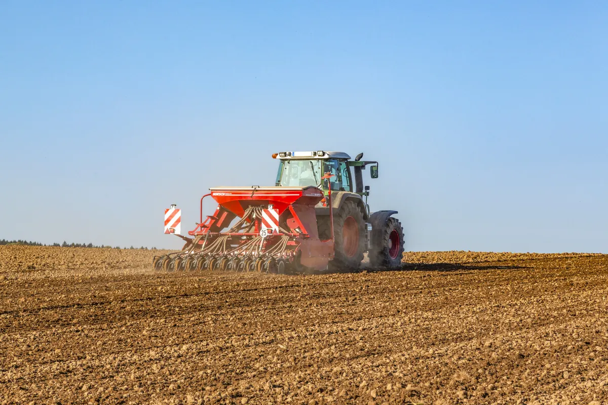 Sembradora Horsch Express TD darrere d'un tractor, sobre un camp de terra oberta amb el cel blau al damunt