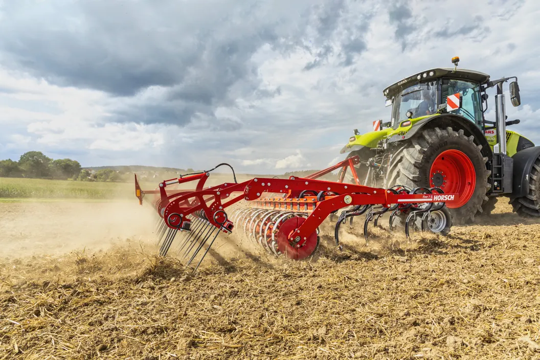 Cultivador Horsch Finer SL treballant amb pols darrere d'un tractor, sota un cel de núvols foscos