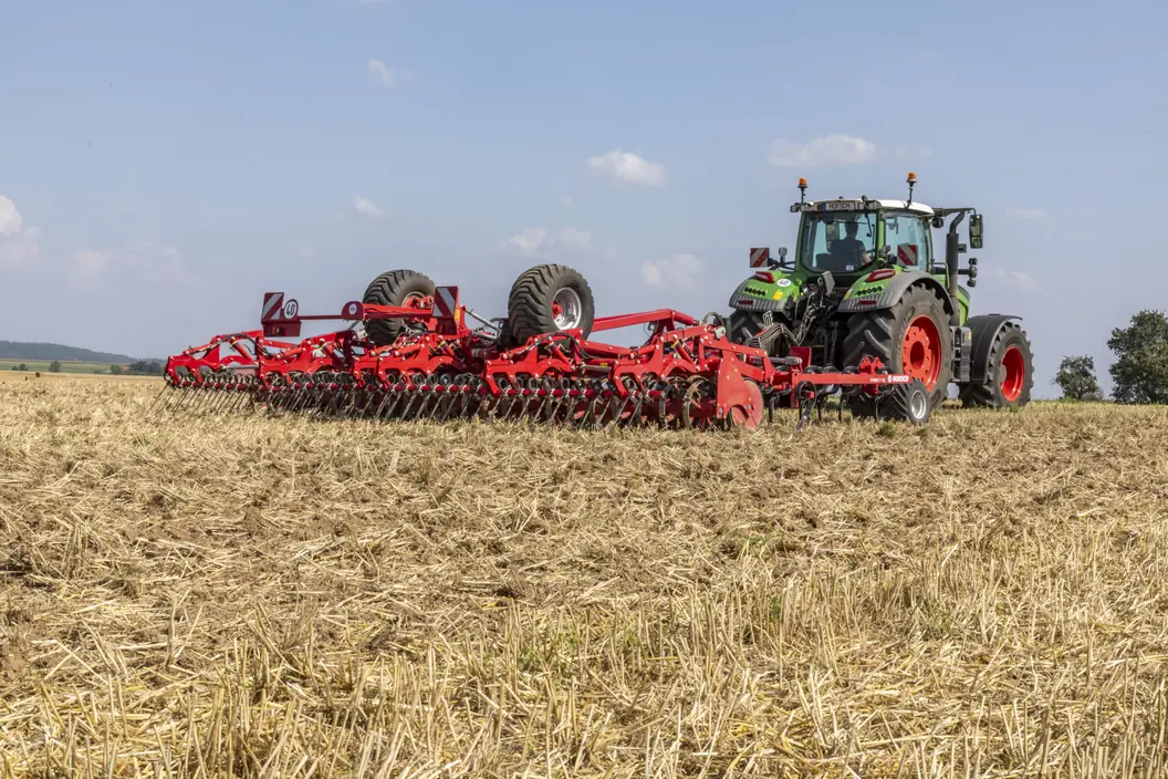 Cultivador Horsch Finer XL desplegat a tota amplada darrere d'un tractor verd, sobre rostoll