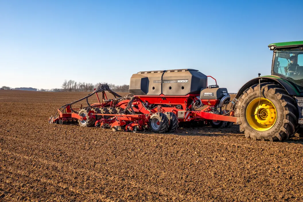 Sembradora Horsch Focus ST F darrere d'un tractor verd de rodes grogues, sobre un camp de terra fosca