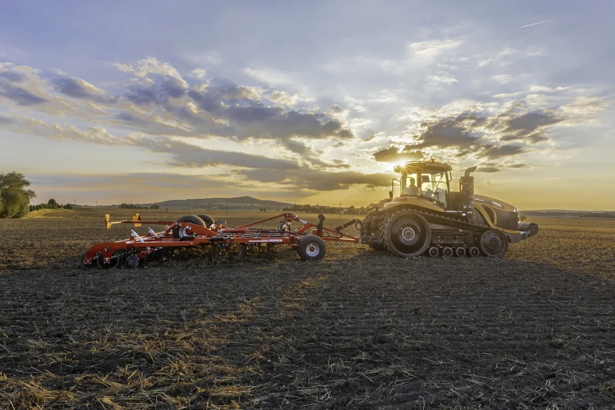 Cultivador Horsch Fortis AS darrere d'un tractor d'erugues al capvespre, amb el cel ennuvolat
