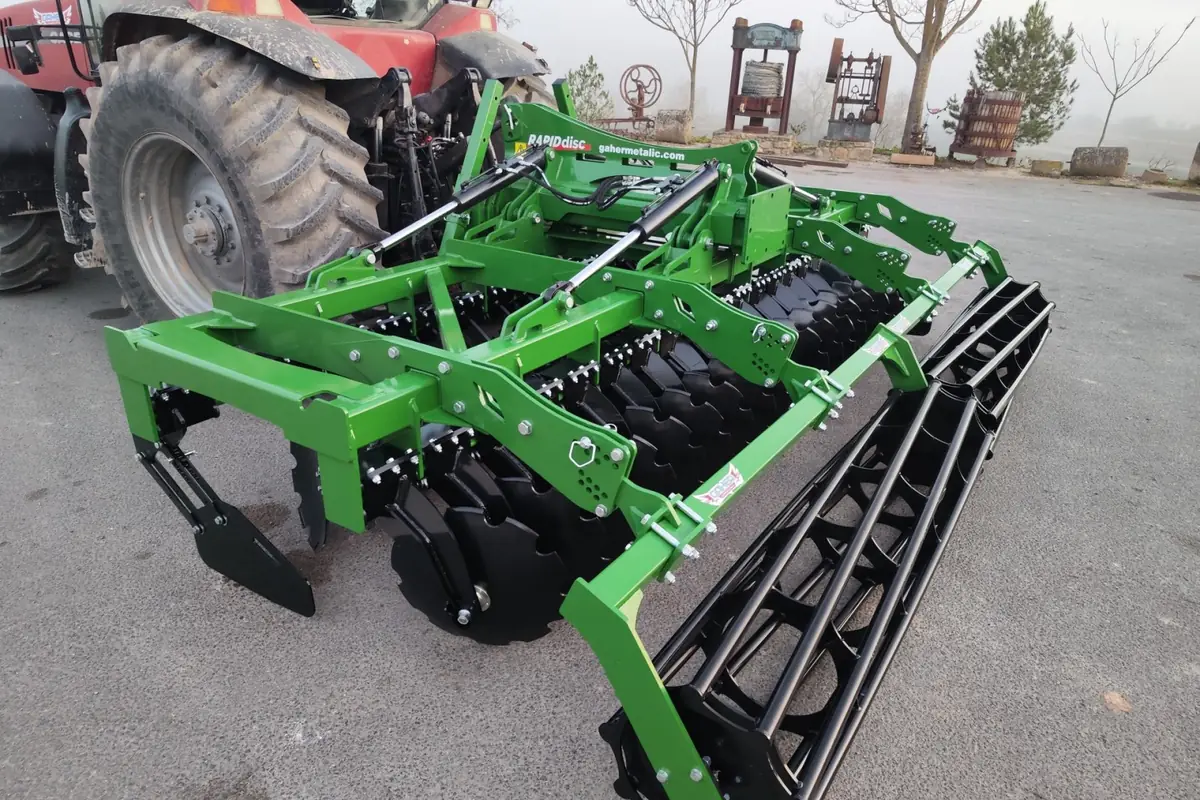 Grada ràpida Gaher de tres quarts sobre asfalt, amb la roda d'un tractor vermell just al darrere i boira al fons