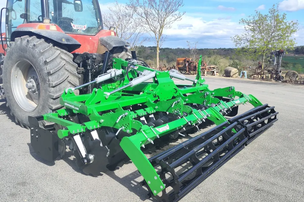Grada ràpida Gaher enganxada a un tractor vermell, de tres quarts pel darrere sobre asfalt, amb el corró de barres en primer pla i arbres al fons
