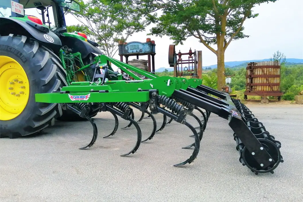 Semixissel plegable Gaher Sèrie Rapid desplegat darrere d'un tractor de rodes grogues, sobre asfalt, amb arbres i cel al fons