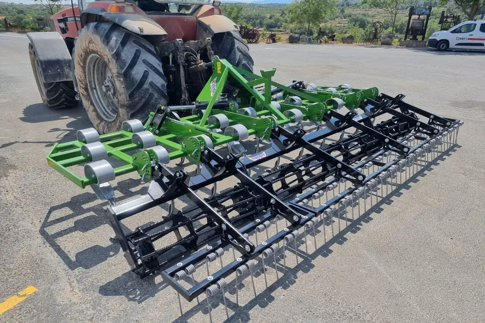 Vibrocultor Gaher desplegat sobre asfalt darrere d'un tractor vermell, amb el rasclet de barres al final