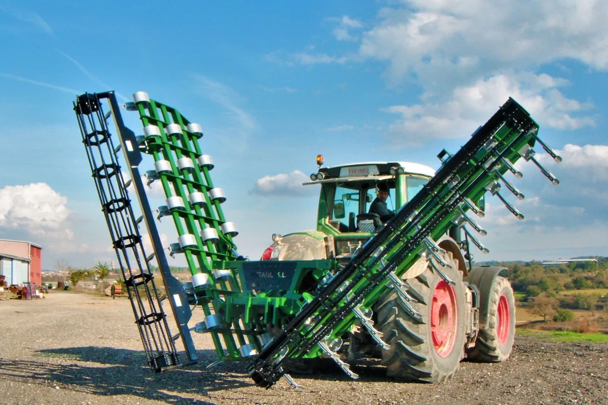 Vibrocultor Gaher enganxat a un tractor verd, amb les ales plegades cap amunt i el cel al fons
