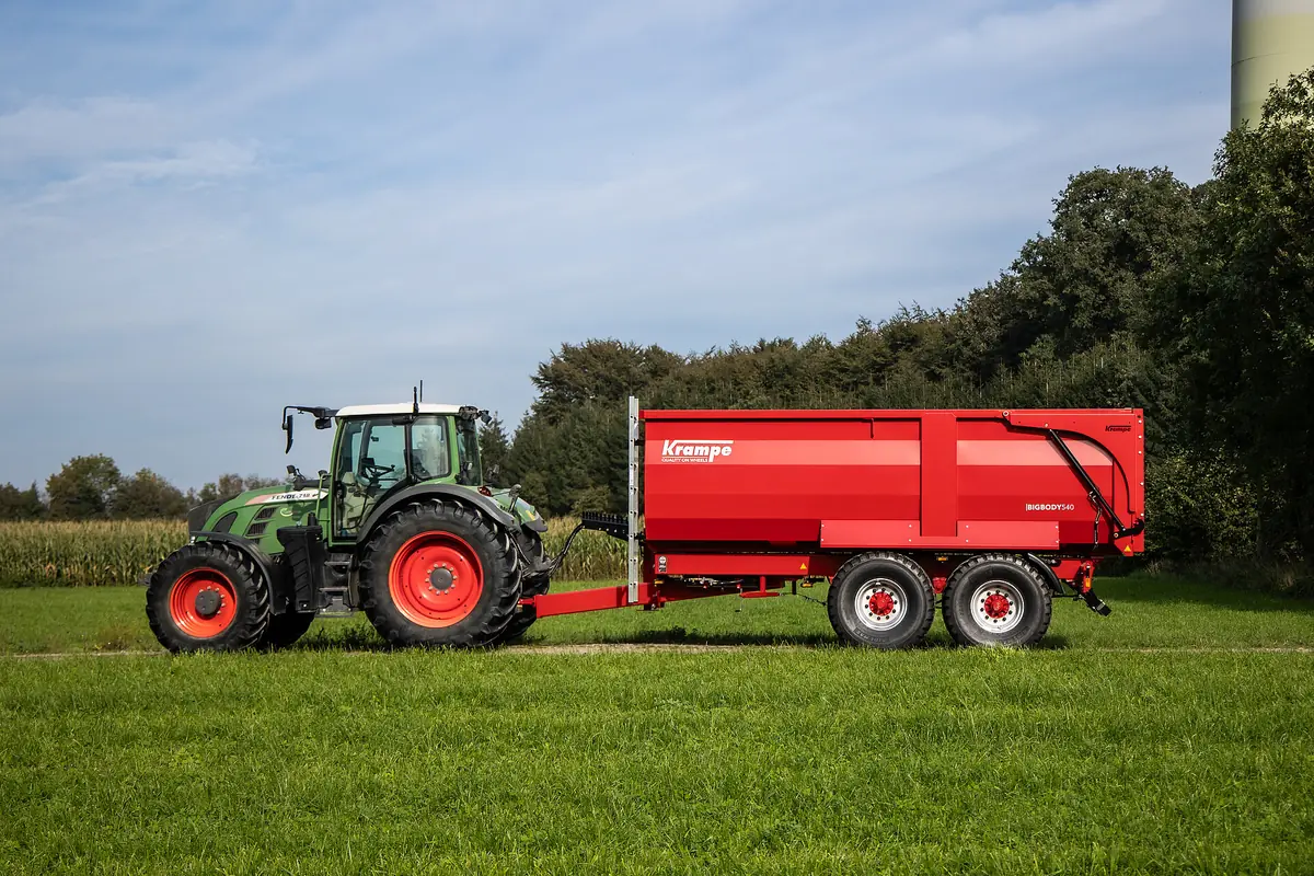 Tractor verd estirant una banyera Krampe BigBody 540 de dos eixos per un prat, de perfil