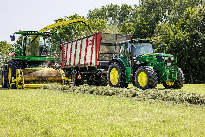 Picadora i tractor verds amb un remolc Krampe Radium 830 en un prat amb fileres d'herba