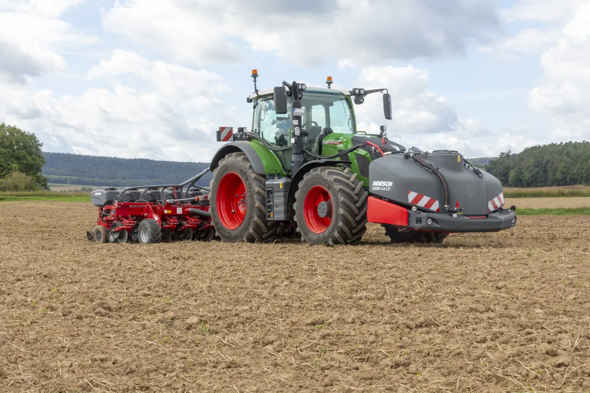 Dipòsit davanter Horsch Leeb 1.4 CT al davant d'un tractor verd, amb una sembradora de precisió al darrere, en un camp de terra treballada