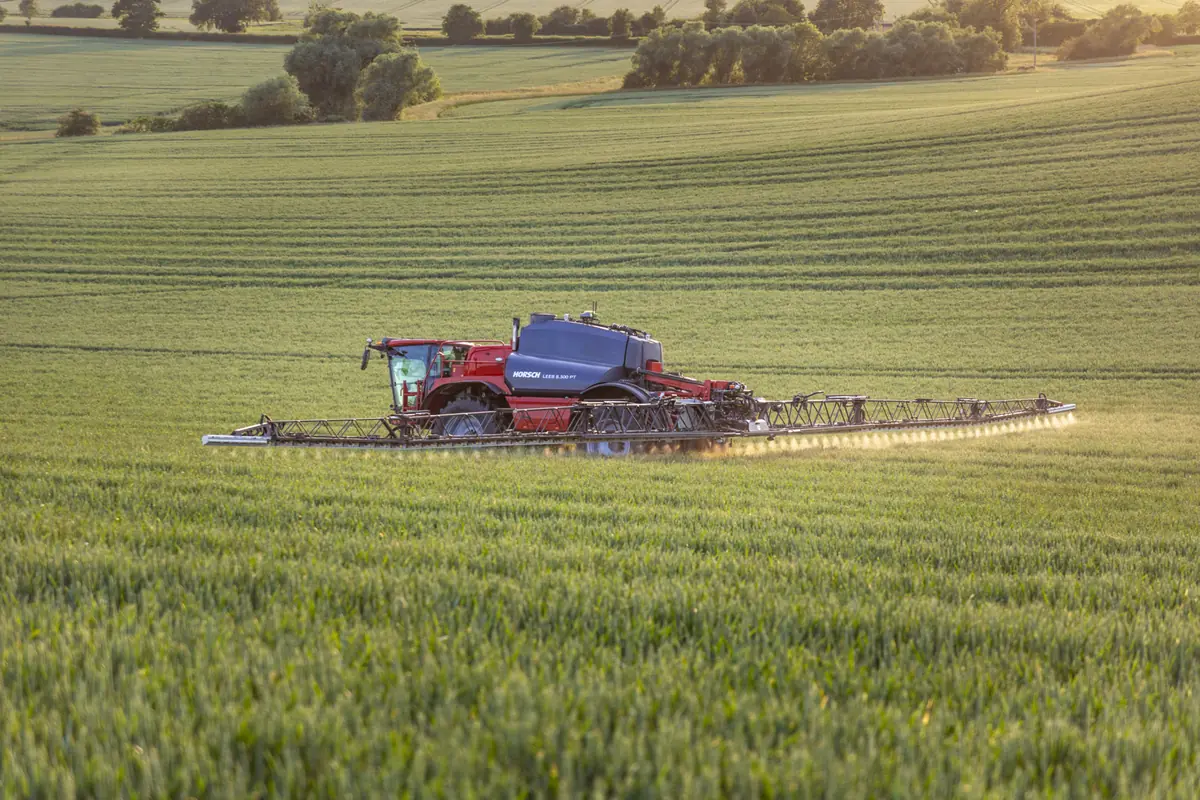 Polvoritzador autopropulsat Horsch Leeb 8.300 PT amb la barra desplegada, ruixant un camp de cereal verd amb la llum baixa