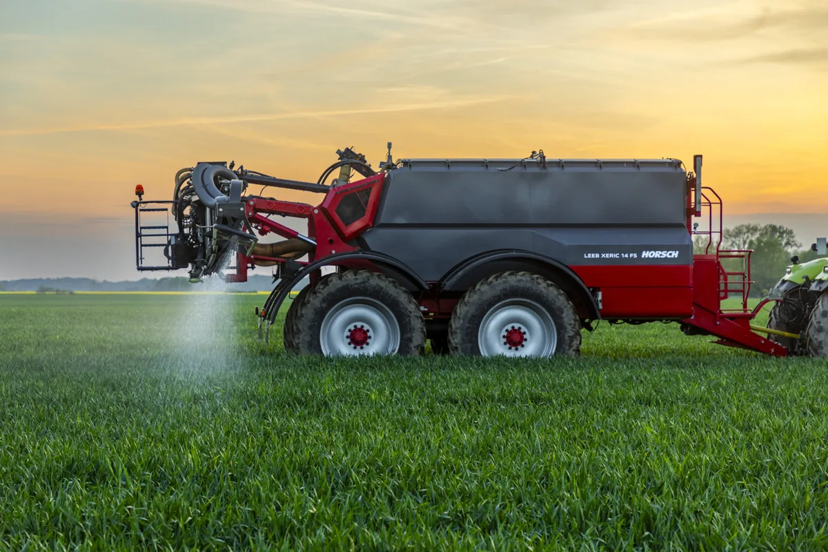 Adobadora pneumàtica arrossegada Horsch Leeb Xeric 14 FS escampant adob en un camp de cereal verd, amb el cel daurat de fons