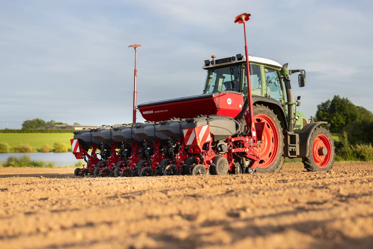 Sembradora Horsch Maestro AX darrere d'un tractor verd, en un camp treballat amb una bassa al fons