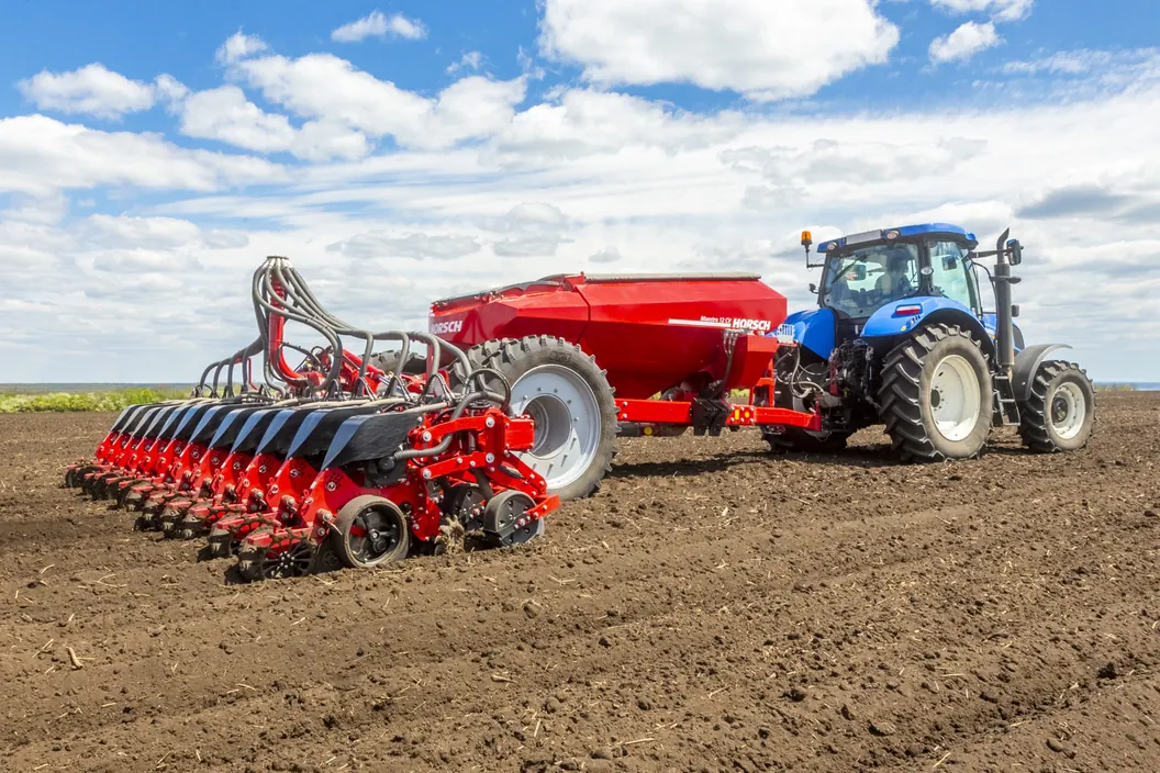 Sembradora Horsch Maestro CV amb una llarga filera d'elements de sembra i la tremuja vermella, amb un tractor blau