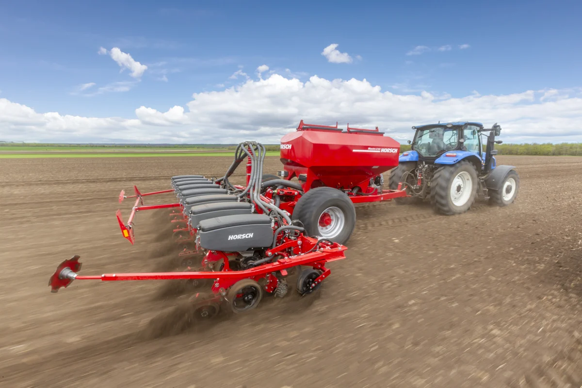 Sembradora Horsch Maestro DV en moviment darrere d'un tractor blau, sobre terra acabada de treballar