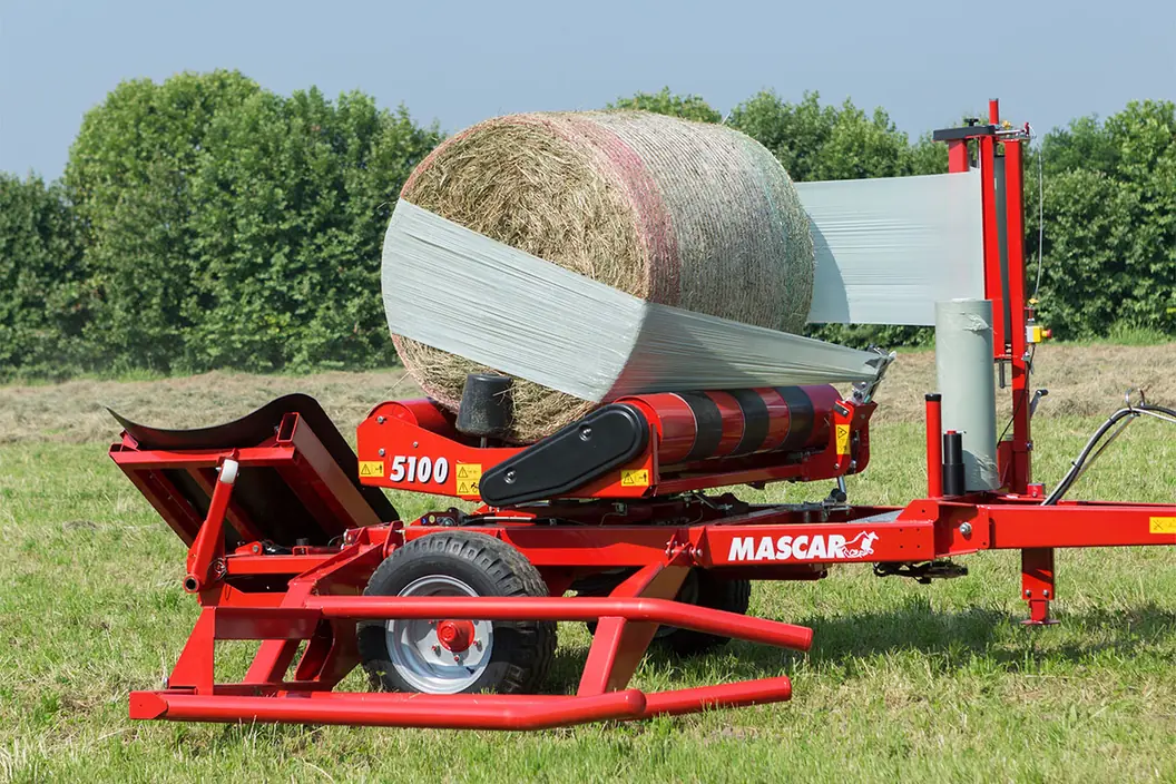 Encintadora Mascar 5100 remolcada embolicant una bala d'herba sobre els corrons, en un prat