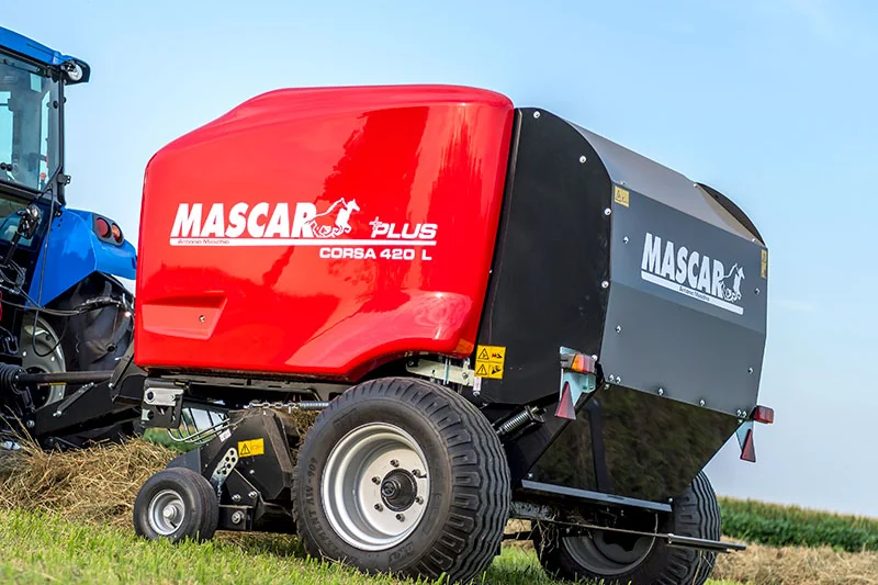 Rotoempacadora Mascar Corsa 420 L en un camp segat, amb un tractor blau enganxat al davant