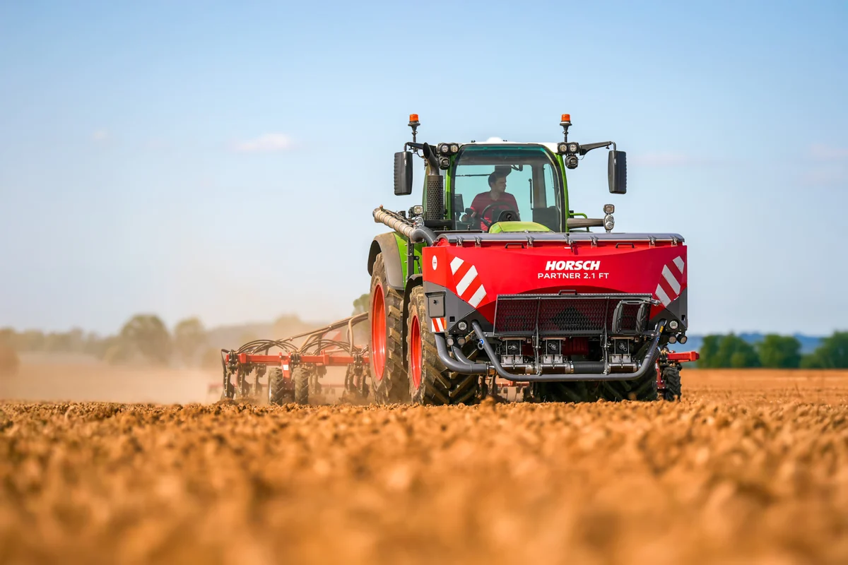 Tremuja davantera Horsch Partner FT muntada al davant d'un tractor verd, amb la pols de la passada al darrere
