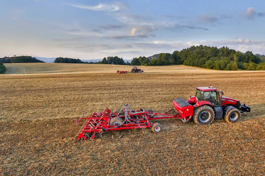 Tremuja Horsch Partner HT darrere d'un tractor vermell, en un camp de rostoll amb els boscos al fons
