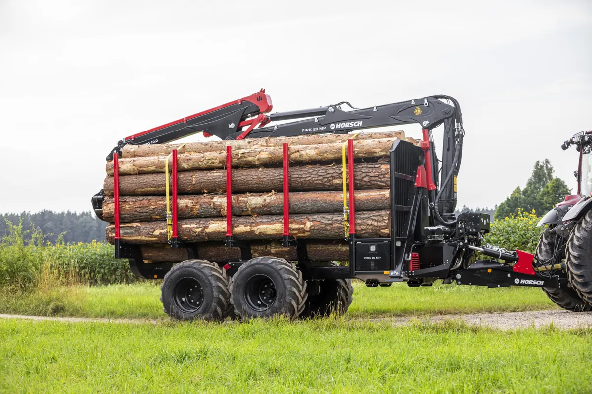 Remolc forestal Horsch Pirk MP carregat de troncs, enganxat a un tractor en un camí de prat