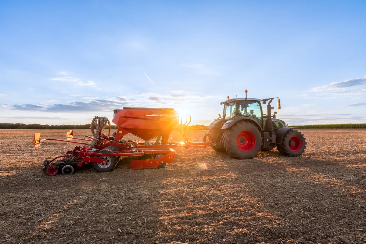 Sembradora Horsch Pronto DC darrere d'un tractor al capvespre, amb el sol arran de terra