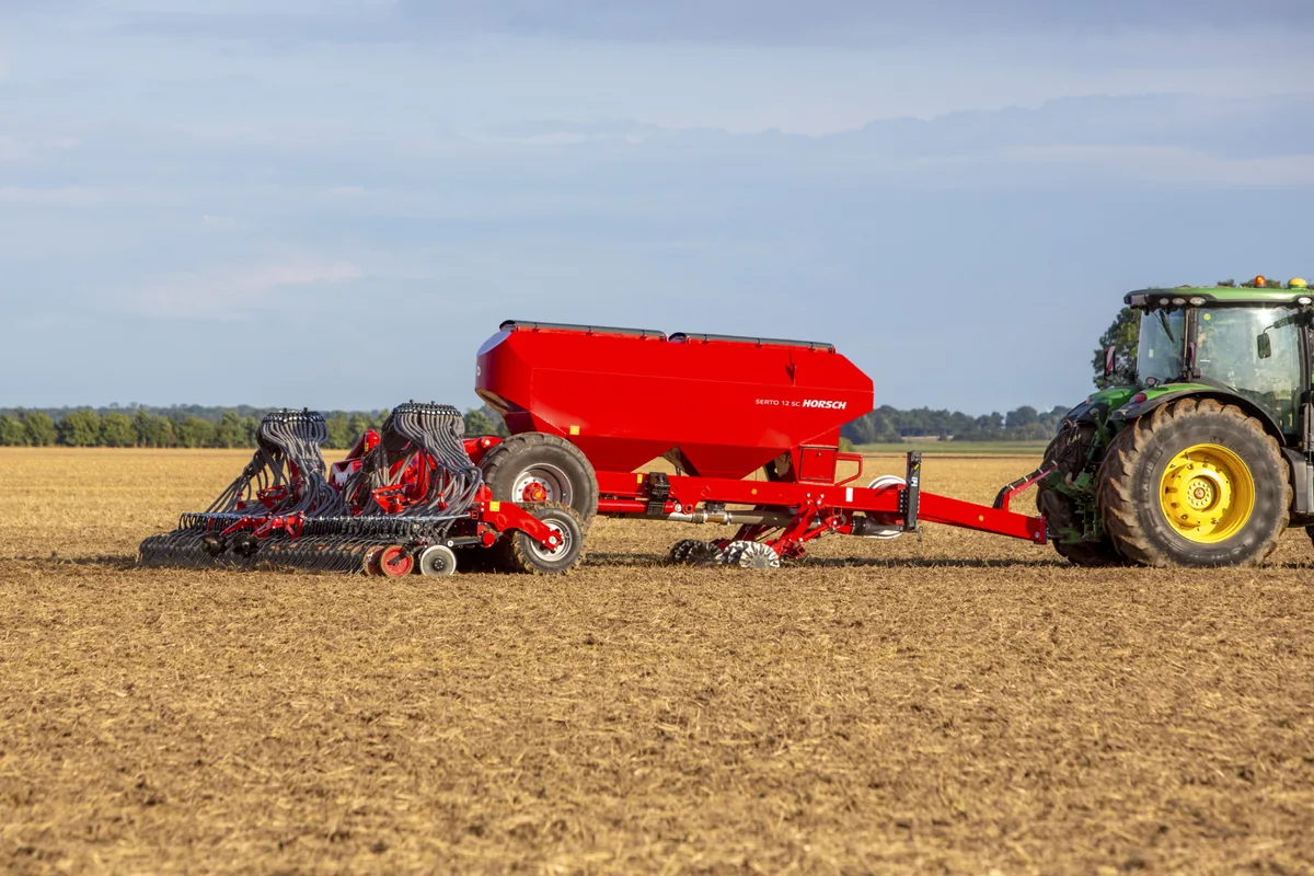 Sembradora Horsch Serto SC amb la tremuja vermella, darrere d'un tractor verd sobre terra treballada