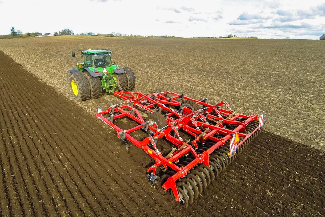 Vista aèria d'un cultivador Horsch Terrano FM desplegat a tota amplada, obrint la terra al costat de la franja ja treballada