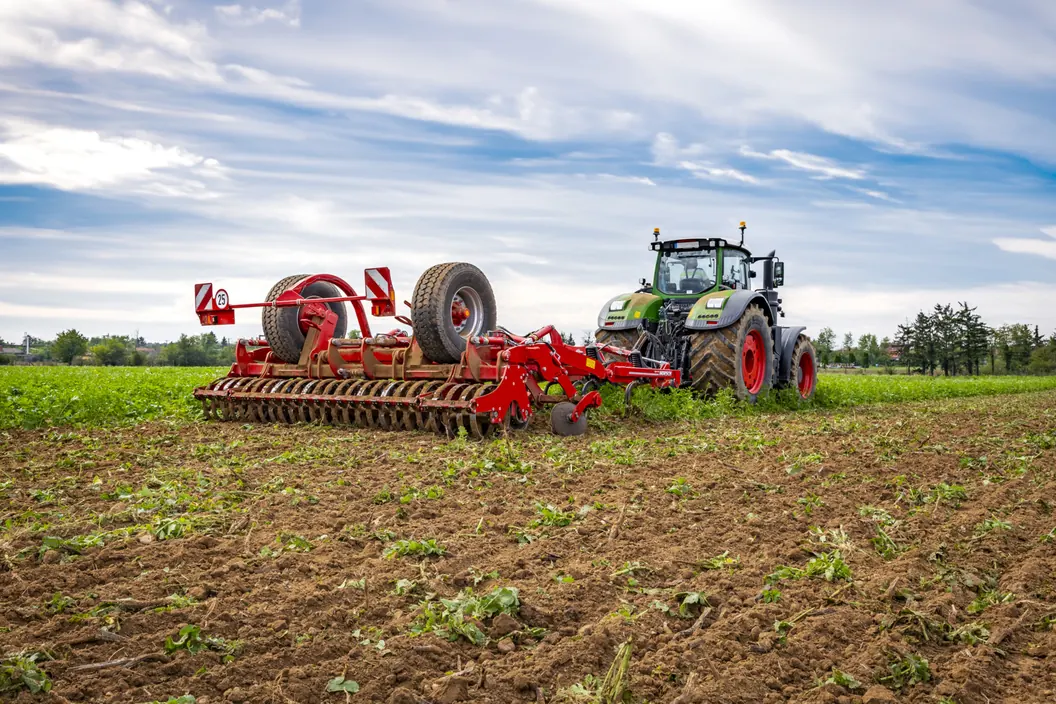 Cultivador Horsch Tiger AS desplegat darrere d'un tractor verd, sobre un camp acabat de treballar i amb el cel obert