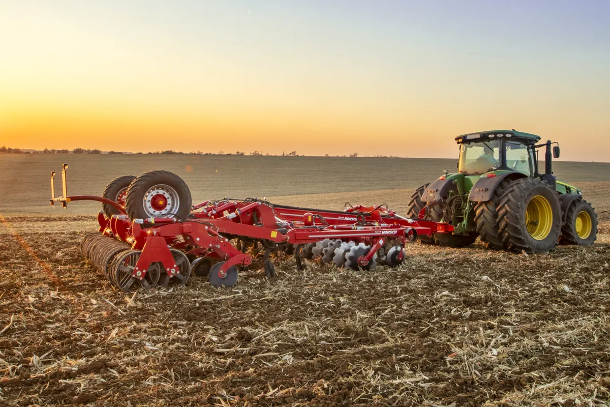 Cultivador Horsch Tiger MT arrossegat per un tractor sobre rostoll, amb la llum baixa de la tarda