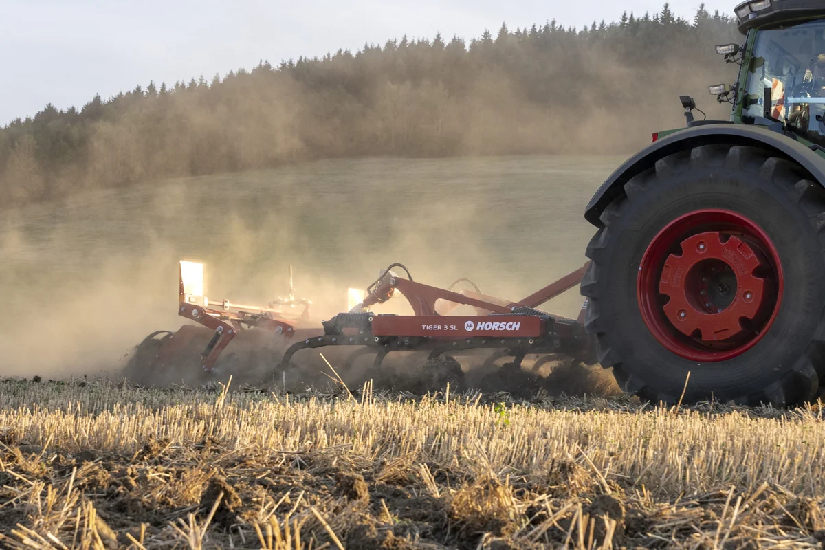 Cultivador Horsch Tiger SL treballant entre un núvol de pols, amb la roda del tractor en primer terme