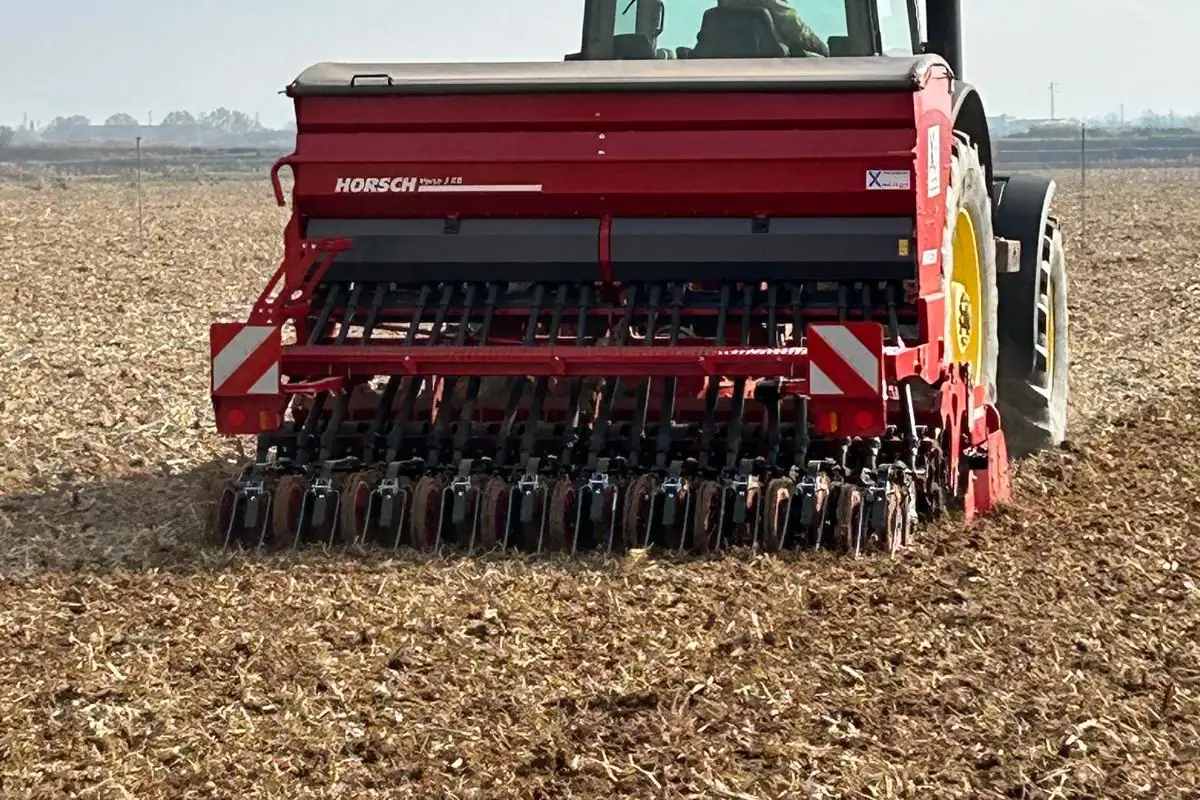 Sembradora Horsch Versa 3 KR vermella vista des del darrere, amb la tremuja, les relles i les rodes de pressió, sembrant sobre rostoll darrere d'un tractor