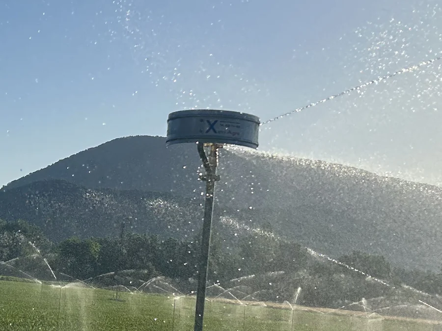 El capçal d'un aspersor regant damunt del seu tub, amb l'adhesiu de XeviAgro i més aspersors regant al fons
